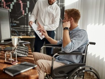 Young male office worker in a wheelchair discussing financial data with his colleague while working together in the office.